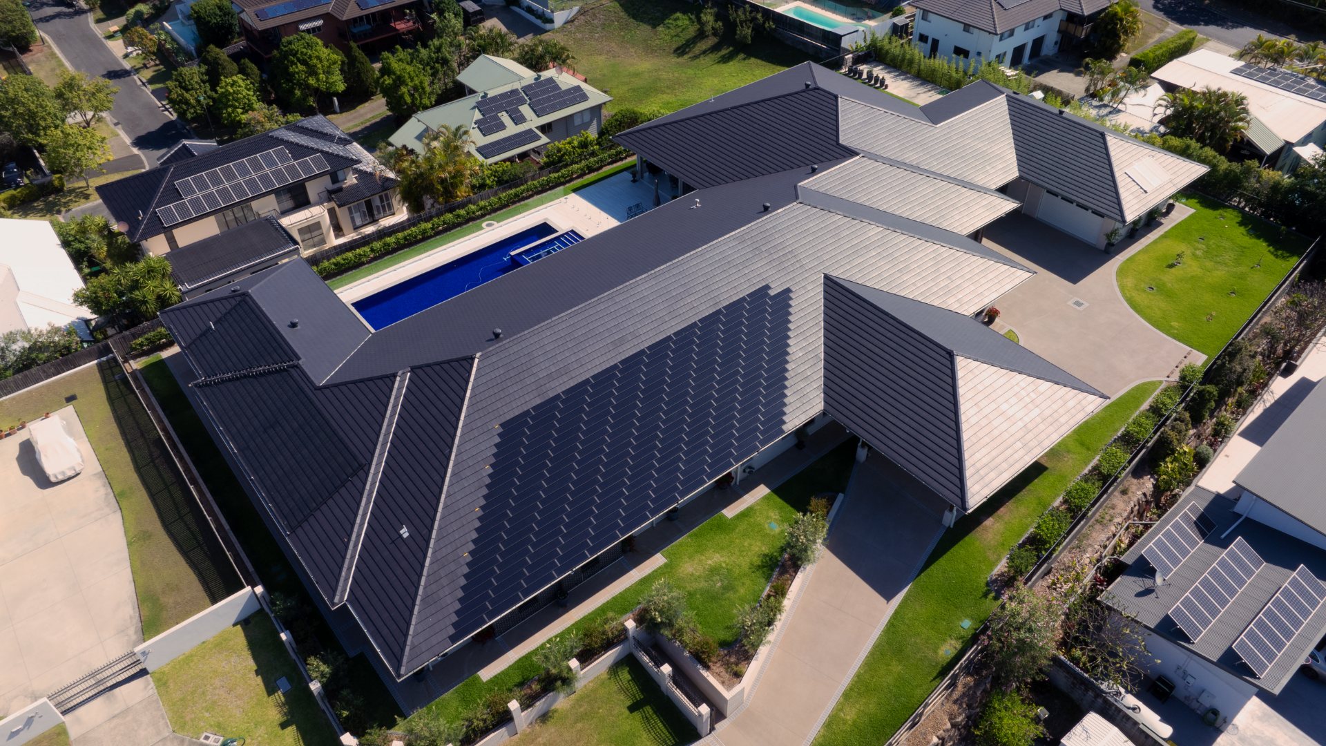 Aerial view of a modern Australian home with integrated solar roof tiles covering a large tiled roof, showing a seamless roofline and backyard pool.