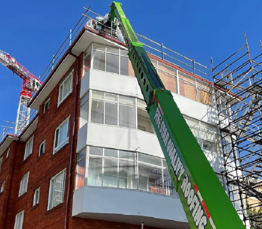 Construction lift reaches workers replacing metal roof tiles.